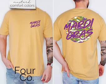May include: Mustard-colored t-shirt with the text "Mardi Gras" in purple on the front and back. The back design features a camouflage circle with the same text. The shirt is a comfort color.