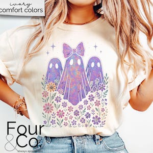 Puede incluir: Camiseta color crema con un dise&ntilde;o de tres fantasmas morados y flores. El fantasma central tiene un lazo. El texto "Four & Co" est&aacute; en la parte inferior de la camiseta. Las palabras "ivory comfort colors" est&aacute;n en la parte superior.