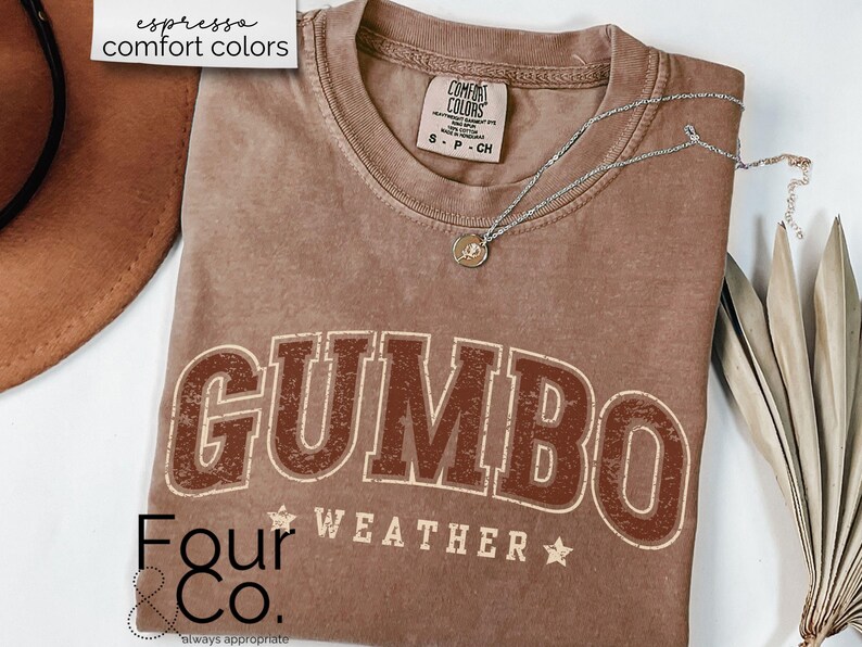 May include: A brown t-shirt with the text "GUMBO WEATHER" in a vintage style font. The shirt also has the text "Four & Co. always appropriate" printed on the bottom.