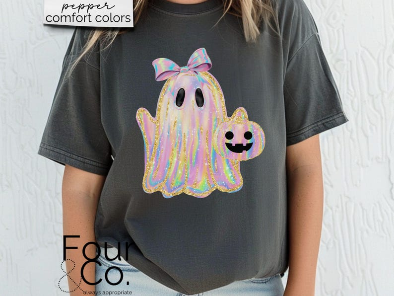 May include: A dark gray t-shirt with a holographic iridescent ghost holding a pumpkin. The ghost has a pink bow on its head. The text "pepper comfort colors" is in the top left corner of the image.