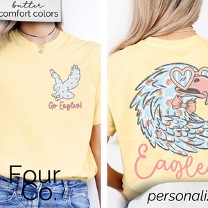 Pu&ograve; includere: T-shirt giallo chiaro con un disegno di aquila. La parte anteriore della maglietta presenta una piccola grafica di aquila e le parole "Go Eagles!". La parte posteriore della maglietta presenta una grafica di aquila pi&ugrave; grande con occhiali da sole a forma di cuore e la parola "Eagles".