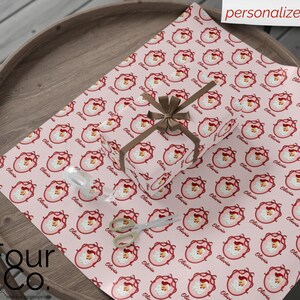 May include: A wrapped gift and wrapping paper featuring a repeating pattern of a Santa Claus face in a pink oval frame with the name "Olivia" in a cursive font. The gift is tied with a brown ribbon. The words "personalize it" are in the top right corner.