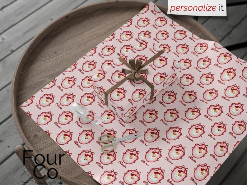 May include: A wrapped gift and wrapping paper featuring a repeating pattern of a Santa Claus face in a pink oval frame with the name "Olivia" in a cursive font. The gift is tied with a brown ribbon. The words "personalize it" are in the top right corner.