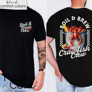 May include: Black comfort colours t-shirt with "Boil & Brew Crew" text and a crawfish graphic. The back features a pot of crawfish and corn with the words "Boil & Brew Crawfish Crew".