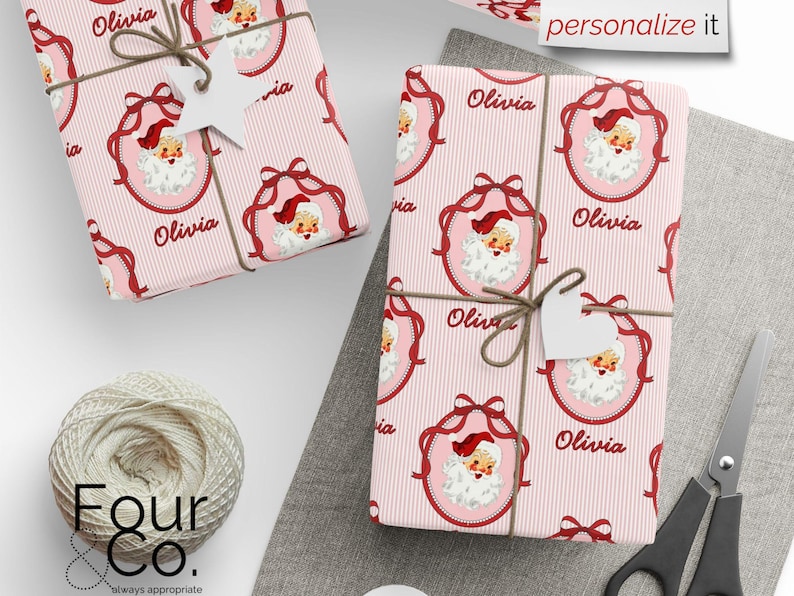 May include: Two wrapped gifts with pink striped paper featuring a Santa Claus design and the name "Olivia." Each package is tied with twine and a white heart-shaped tag. The words "personalize it" are visible.