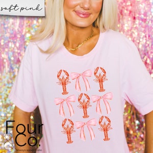 May include: A pink t-shirt with a graphic of red lobsters with pink bows. The text "Four & Co. always appreciate" is at the bottom of the shirt.
