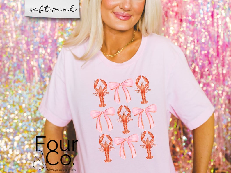 May include: A pink t-shirt with a graphic of red lobsters with pink bows. The text "Four & Co. always appreciate" is at the bottom of the shirt.