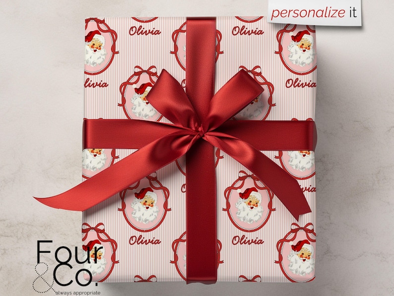 May include: A wrapped gift with a red ribbon and bow. The wrapping paper features a repeating pattern of Santa Claus faces in pink frames with the name "Olivia" and a striped background. The words "personalize it" are in the top right corner.