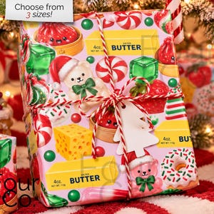 May include: A gift wrapped in light pink paper featuring a repeating pattern of cartoon bears in Santa hats, red dumplings, yellow butter sticks labeled 4oz, green cubes, and donuts. The package is tied with red and white twine and a tree-shaped tag.