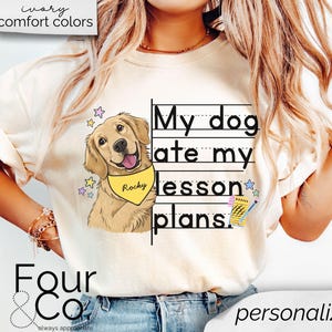 May include: A white t-shirt with the text "My dog ate my lesson plans." printed on it. A cartoon image of a golden retriever dog wearing a yellow bandana with the name "Rocky" is next to the text. The shirt is being worn by a person with long blonde hair.