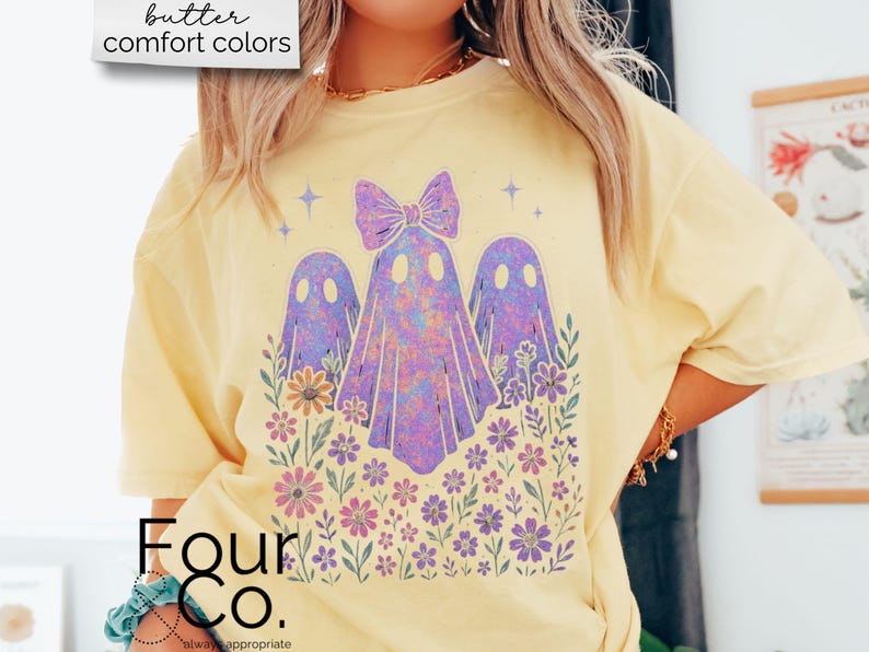 Puede incluir: Camiseta amarilla clara con un gr&aacute;fico de tres fantasmas morados con un lazo, rodeados de flores. El texto "butter comfort colors" est&aacute; en la esquina superior izquierda. La marca "Four Co." est&aacute; en la parte inferior.