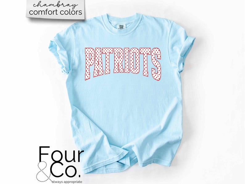 May include: Light blue t-shirt with the word "PATRIOTS" in red polka dot letters. The shirt has rolled-up sleeves and the text "chambray comfort colors" is in the upper left corner. The logo "Four & Co." is in the lower left corner.