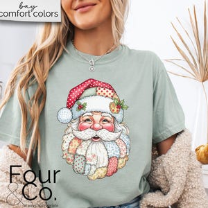 May include: A light green t-shirt featuring a colorful Santa Claus graphic. The Santa Claus design has a patchwork style hat and beard. The text "bay comfort colors" is at the top left. The text "Four & Co. always appropriate" is at the bottom left.