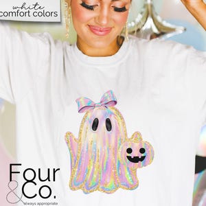May include: White t-shirt with a holographic iridescent ghost holding a pumpkin. The ghost has a pink bow on its head. The text "Four & Co. always appropriate" is at the bottom of the shirt.