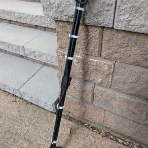 May include: A black metal detector with a circular search coil and a long, adjustable stem. White cable ties secure the wires to the stem. The detector is leaning against a stone wall and concrete steps.