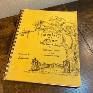 May include: A spiral-bound book with a yellow cover featuring a black ink illustration of a large tree and two stone pillars. The text reads: Musings of a Hermit by Clarke A. Willcox with Historical Sketches of the Waccamaw Neck. Seventh Edition.
