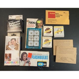 May include: A collection of vintage photography supplies, including Polaroid film cleaner, flashcubes, flashbulbs, lens cleaning paper, and film. The items are in their original packaging, with retro graphics and text.