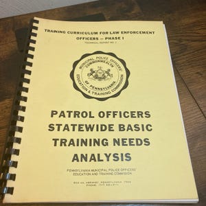 May include: A spiral-bound training manual with a pale yellow cover titled Training Curriculum for Law Enforcement Officers - Phase I, Technical Report No. 2, featuring the Commonwealth of Pennsylvania Municipal Police Officers seal.