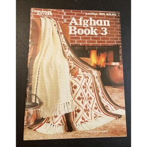 May include: A softcover craft instruction booklet titled Afghan Book 3 by Leisure Arts. The cover features a photograph of two crocheted afghans with fringe, one cream-colored with cable textures and one white with brown diamond patterns.