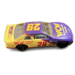 May include: A toy race car with a yellow and purple color scheme. The car features the number 62 on the roof and the number 29 on the side. The words "WCW World Championship Wrestling" are printed on the car.