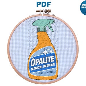 Puede incluir: Un patrón de punto de cruz en un bastidor de madera que muestra una botella de spray naranja con una etiqueta azul claro. La etiqueta muestra el texto Opalite, Magical Results! y Don't Sweat It! con iconos de estrellas blancas sobre tela azul.