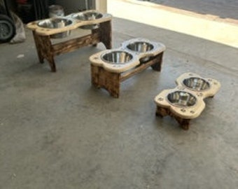May include: Three wooden dog food bowls with stainless steel bowls. The bowls are elevated on wooden stands of varying heights. The stands are made of natural wood with a rustic finish.