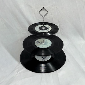 May include: Three-tiered cake stand made from black vinyl records with a silver metal stand.