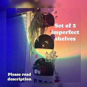 May include: Set of three imperfect shelves, with a rainbow light projection on the wall behind them. The shelves are made of wood and have a rustic look. The shelves are decorated with plants, candles, and other decorative items. The text "Set of 3 imperfect shelves" is written on the wall.