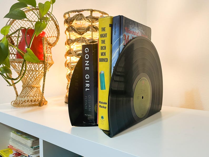 May include: A pair of black vinyl record bookends holding up three books. The book titles are "Gone Girl" by Gillian Flynn, "The Night the Rich Men Burned" by Malcolm Mackay, and "The Mysterious Mr. Quin" by  Agatha Christie.