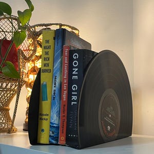 May include: Black vinyl record bookends with a white label that says "Jennifer's Journal". The bookends are holding up four books: "Gone Girl" by Gillian Flynn, "Fear and Loathing in Las Vegas" by Hunter S. Thompson, "Moby Dick" by Herman Melville, and "The Night the Rich Men Burned" by Malcolm Mackay.
