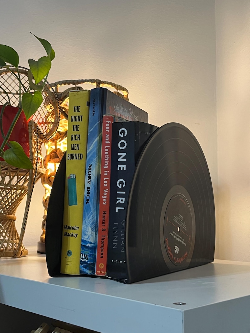 May include: Black vinyl record bookends with a white label that says "Jennifer's Journal". The bookends are holding up four books: "Gone Girl" by Gillian Flynn, "Fear and Loathing in Las Vegas" by Hunter S. Thompson, "Moby Dick" by Herman Melville, and "The Night the Rich Men Burned" by Malcolm Mackay.