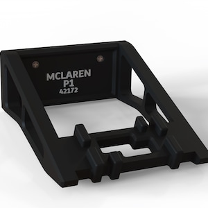 May include: Black wall mount display stand for a McLaren P1 model car. The stand has a rectangular base with a cutout for the car and a raised platform for the car to sit on. The stand is made of black plastic and has a silver label that reads "McLaren P1 42172".