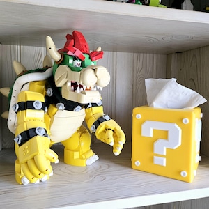 May include: A yellow and green Lego Bowser figure with a red shell and a question mark block tissue box.