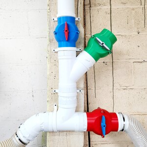 May include: Three white plastic pipes with three different colored valves. The valves are blue, green, and red. The pipes are connected to each other and to a white hose.