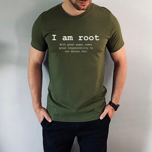 May include: Olive green t-shirt with the text "I am root" in white, followed by a quote about responsibility. The shirt is a crew neck style and is being worn.