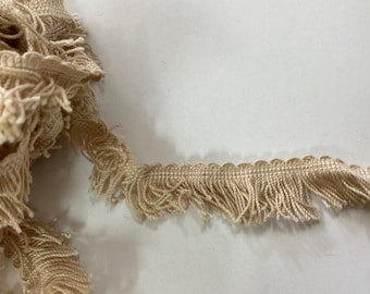 May include: Beige fringe trim with a scalloped edge. The fringe is made of a soft, woven fabric.
