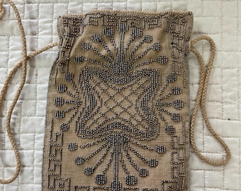 May include: A beige beaded bag with a silver geometric design and a silver fringe. The bag has a drawstring closure and a long strap.