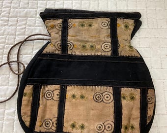 May include: A black drawstring bag with a tan fabric panel featuring a repeating pattern of circles. The bag is made of a sturdy fabric and has a simple design.
