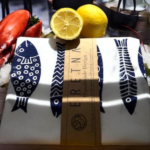 May include: A white kitchen towel with a blue fish design. The towel has a brown label that says "Eretna Handmade Design".