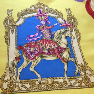 Puede incluir: Pa&ntilde;uelo de seda con una ilustraci&oacute;n detallada de una persona montada a caballo, enmarcada en un borde ornamentado. El dise&ntilde;o presenta un fondo azul, un borde amarillo y detalles en rojo, rosa y dorado.