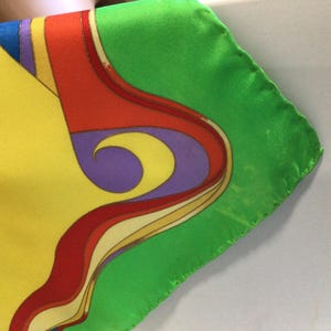 Puede incluir: Un pa&ntilde;uelo de seda colorido con un dise&ntilde;o vibrante. El pa&ntilde;uelo presenta un fondo amarillo con una figura dorada y negra adornada, y un borde verde. El dise&ntilde;o incluye formas curvas rojas, moradas y amarillas.