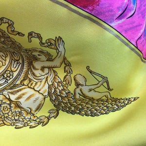 Puede incluir: Un pa&ntilde;uelo de seda con fondo amarillo y dise&ntilde;o con figuras cl&aacute;sicas y elementos florales en oro y crema. El pa&ntilde;uelo tiene detalles en rosa y rojo.