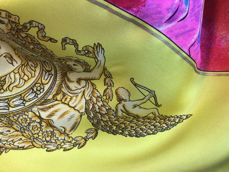 Puede incluir: Un pa&ntilde;uelo de seda con fondo amarillo y dise&ntilde;o con figuras cl&aacute;sicas y elementos florales en oro y crema. El pa&ntilde;uelo tiene detalles en rosa y rojo.