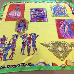 Puede incluir: Un pa&ntilde;uelo de seda amarillo con borde verde e ilustraciones coloridas. El pa&ntilde;uelo presenta im&aacute;genes enmarcadas de figuras en varias poses, incluyendo bailarines y una mujer con un vestido. El dise&ntilde;o incluye un emblema decorativo y patrones geom&eacute;tricos.