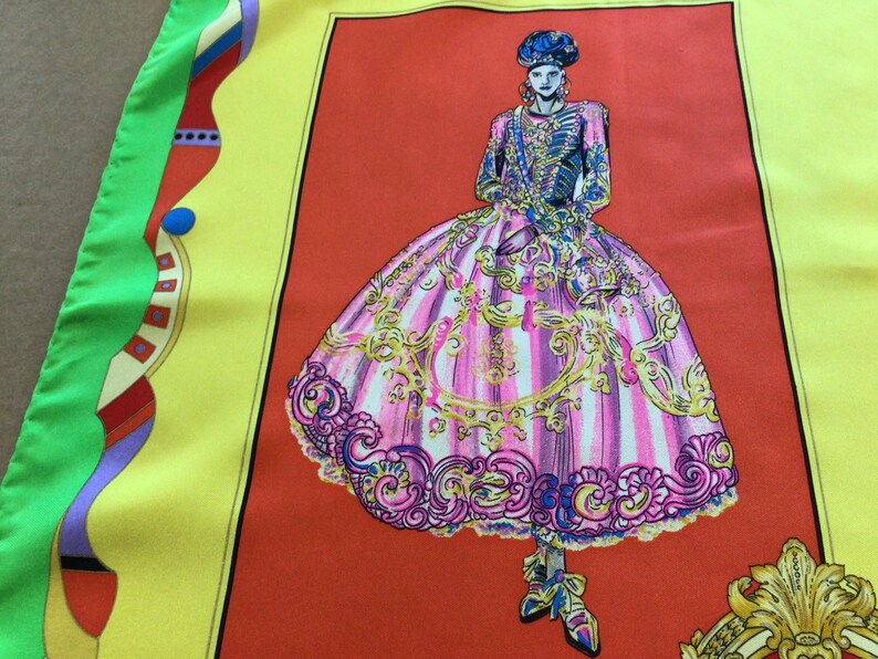 Puede incluir: Pa&ntilde;uelo de seda con una ilustraci&oacute;n de moda de una persona con vestuario hist&oacute;rico. El dise&ntilde;o incluye un vestido a rayas rosas y blancas con adornos dorados, sobre un fondo rojo, enmarcado por bordes amarillos y verdes.