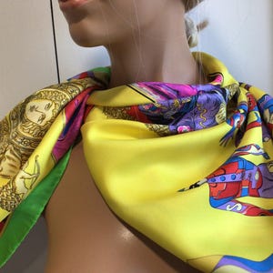 Puede incluir: Un pa&ntilde;uelo de seda amarillo vibrante con ilustraciones y acentos coloridos. El pa&ntilde;uelo presenta una variedad de dise&ntilde;os, incluyendo figuras, patrones y bordes en tonos de rojo, morado, verde y azul. El pa&ntilde;uelo est&aacute; drapeado sobre un maniqu&iacute;.