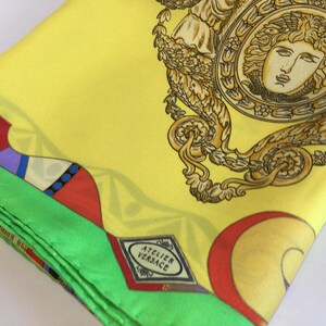 Puede incluir: Un pa&ntilde;uelo de seda amarillo doblado con un borde verde y patrones geom&eacute;tricos coloridos. El pa&ntilde;uelo presenta un dise&ntilde;o de cabeza de Medusa dorada y el logotipo "ATELIER VERSACE".