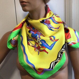 Puede incluir: Un pa&ntilde;uelo de seda amarillo vibrante con un dise&ntilde;o abstracto colorido. El pa&ntilde;uelo presenta un borde verde y azul, con detalles en rojo. El dise&ntilde;o incluye figuras en azul, rojo y morado. Un accesorio elegante.