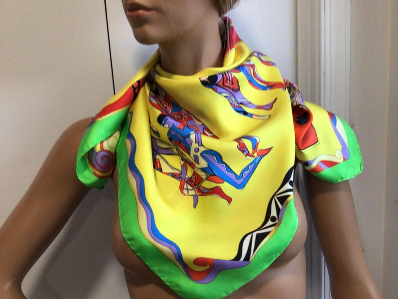 Puede incluir: Un pa&ntilde;uelo de seda amarillo vibrante con un dise&ntilde;o abstracto colorido. El pa&ntilde;uelo presenta un borde verde y azul, con detalles en rojo. El dise&ntilde;o incluye figuras en azul, rojo y morado. Un accesorio elegante.