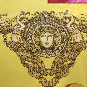Puede incluir: Una tela amarilla con un dise&ntilde;o dorado ornamentado. El dise&ntilde;o presenta un medall&oacute;n central con un rostro, flanqueado por figuras y querubines. La est&eacute;tica general es cl&aacute;sica y decorativa.